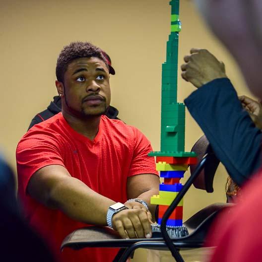 A student assists in building a structure out of plastic blocks for a class